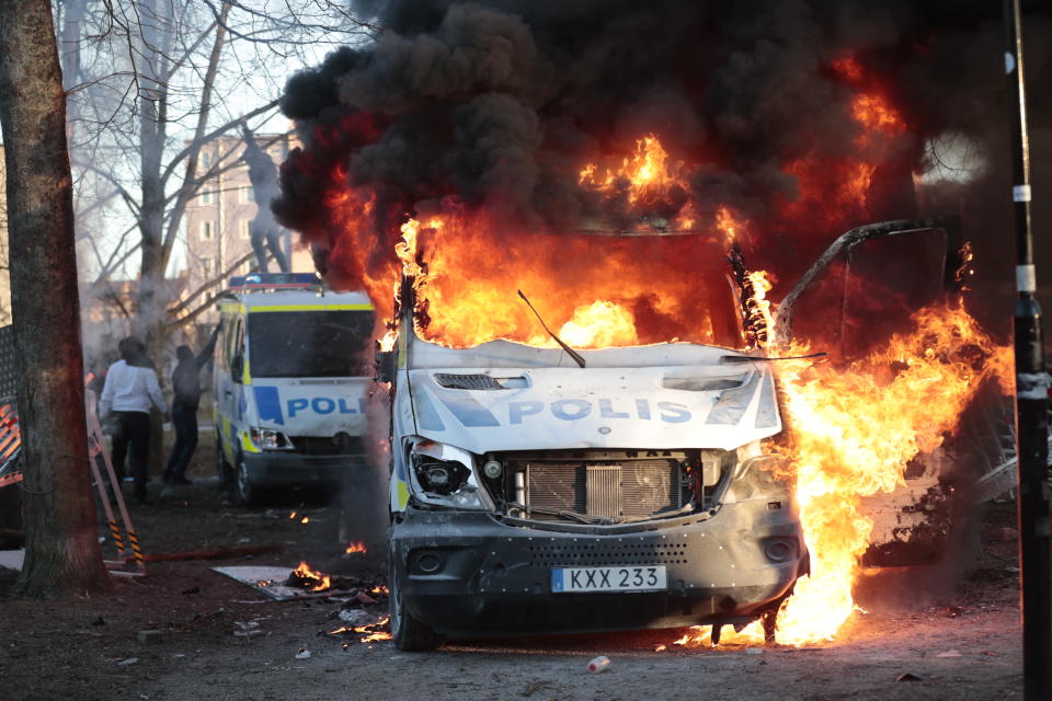 Liekeissä oleva poliisiauto ja mellakoitsijoita tuhoamassa toista poliisiautoa.