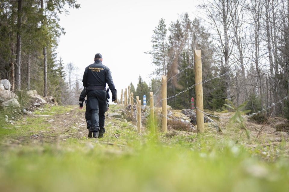 Kaksi rajavartijaa kävelee raja-aukolla piikkilanka-aidan vieressä.