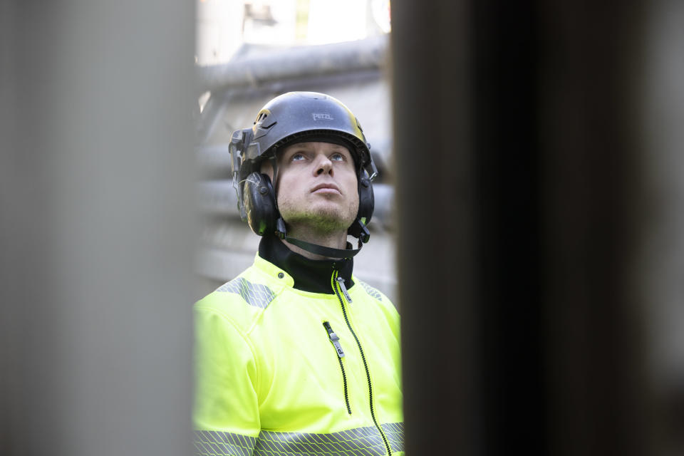 Poraaja Antti Roth katsoo kohti kallioporan yläosaa työvaatteet ja sininen kypärä yllään.