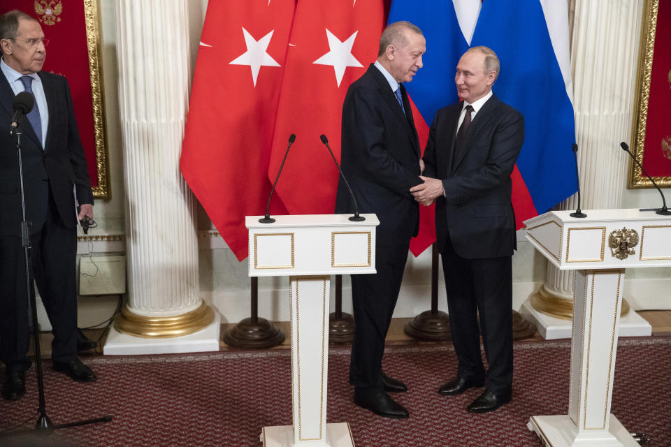 Venäjän ulkoministeri Sergei Lavrov katsoo kuvan oikealta reunalta kun Turkin presidentti Recep Tayyip Erdogan ja Venäjän presidentti Vladimir Putin kättelevät. Takana Turkin ja Venäjän liput. Edessä mikrofonit.