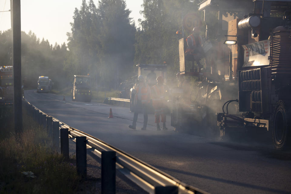 asfalttikone tekemässä asfalttia maantiellä, savun takaa erottuu asfalttityöntekijöitä kävelemässä