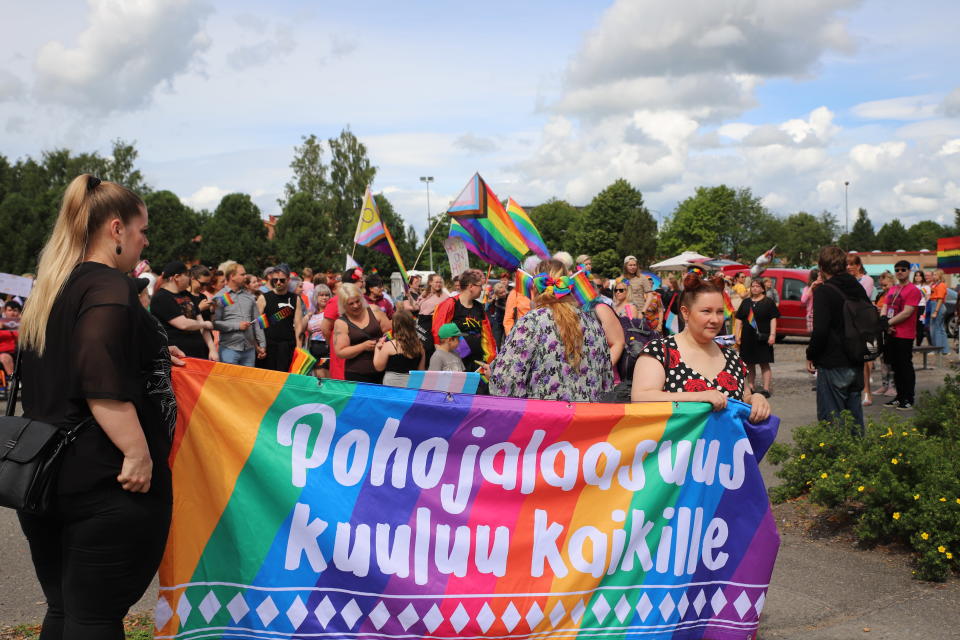 Pride-tapahtumassa liikkuvia ihmisiä Lapualla aurinkoisena kesäisenä päivänä, kuvissa näkyy sateenkaarilippuja. Kuvituskuvaa.