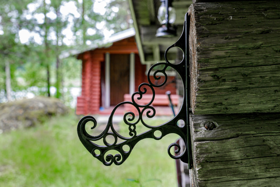 Koristeellinen koukku hirsiseinän päädyssä. Taustalla näkyy rantasauna.