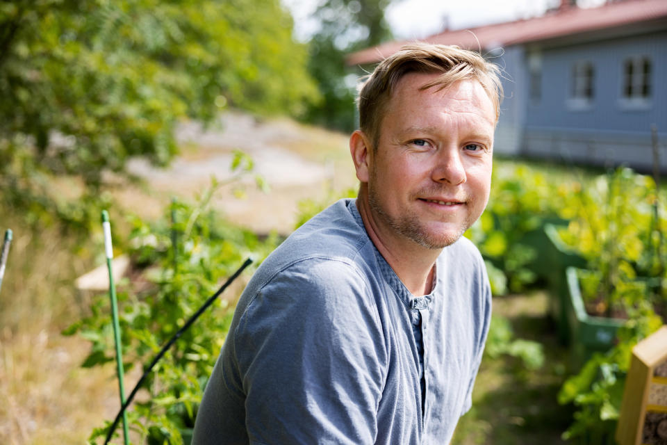 Mies katsoo kameraan ulkona taustallaan kasvillisuutta.