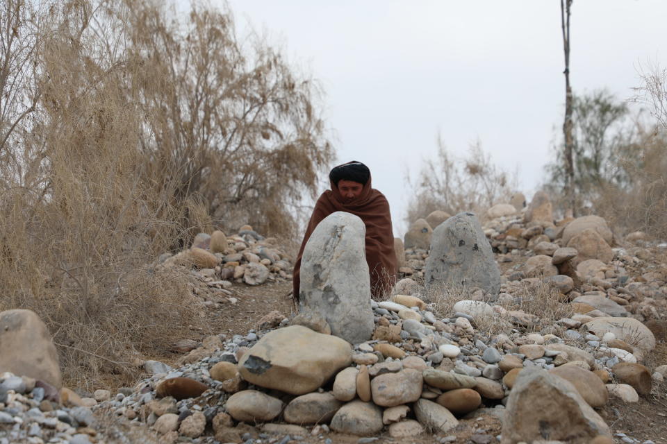  Shaaliin kääriytynyt mies istuu suuren kiven edessä hautausmaalla.