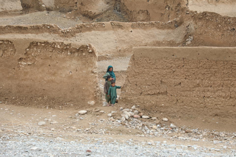Nainen ja kaksi lasta seisoo savitiilistä rakennetun aidan aukossa.