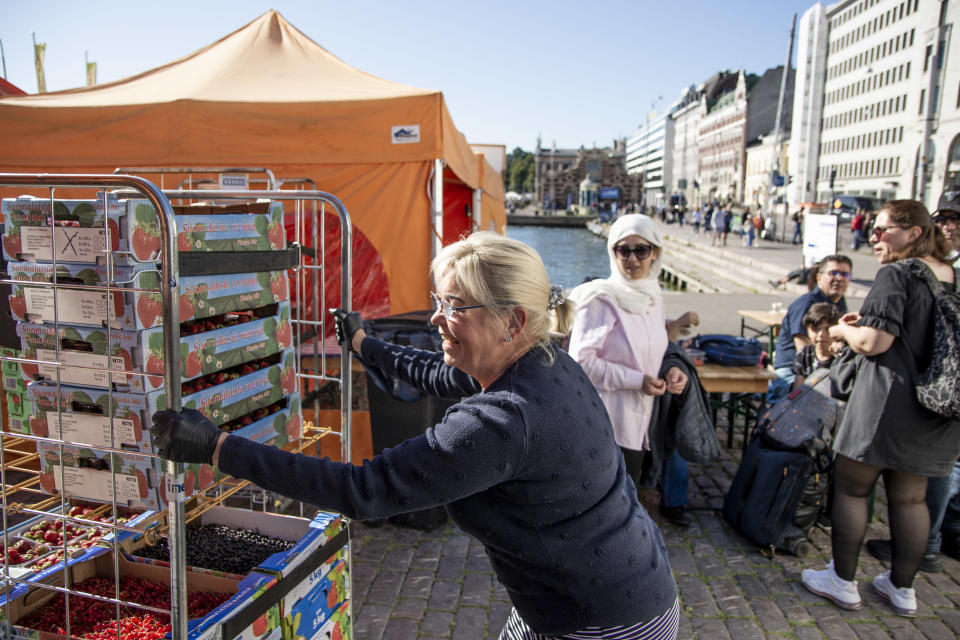 Tuula Matero työtnää marjoja rullakossa hymyillen. Turistit katsovat vierestä.