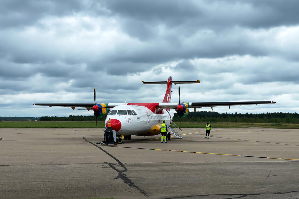 Danish air transport -yhtiön (DAT) punavalkoinen ATR-potkuriturbiinikone Kajaanin lentokenttätasolla, taustalla taivaalla synkkiä sadepilviä.