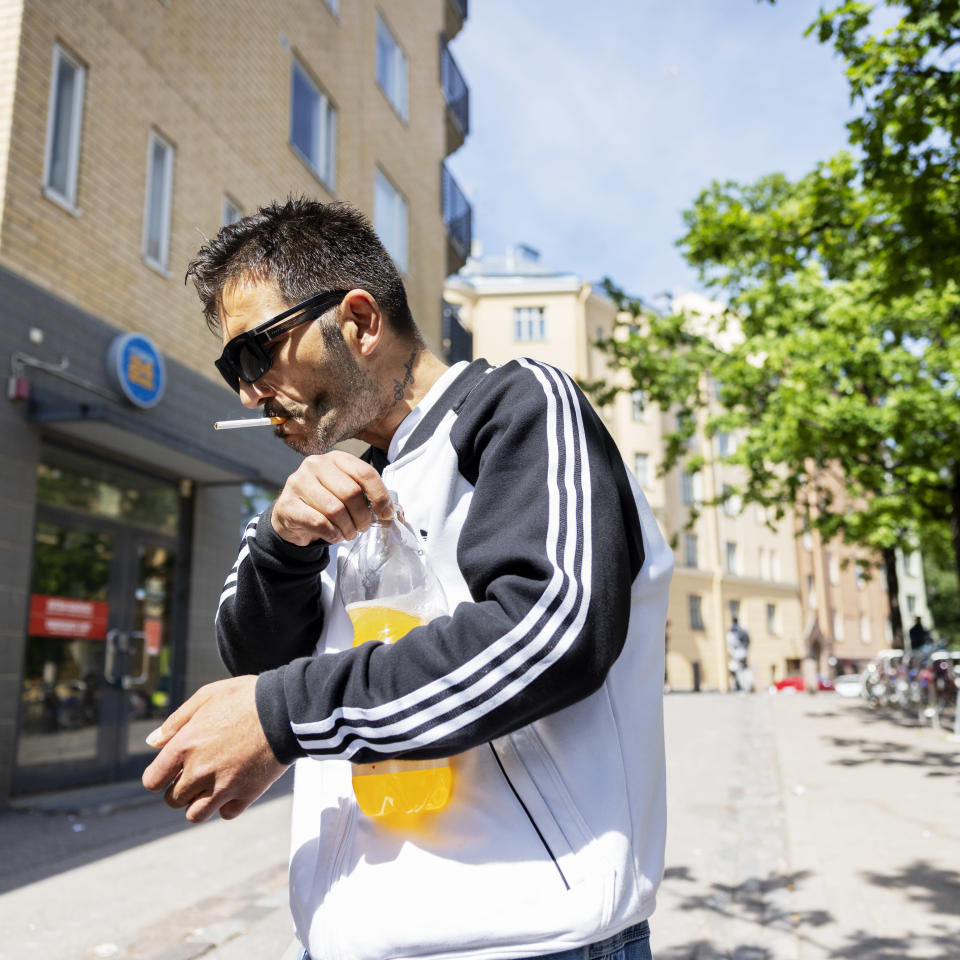 A person smokes a cigarette and opens a soda bottle with sunglasses on in Vaasanpuistiko.